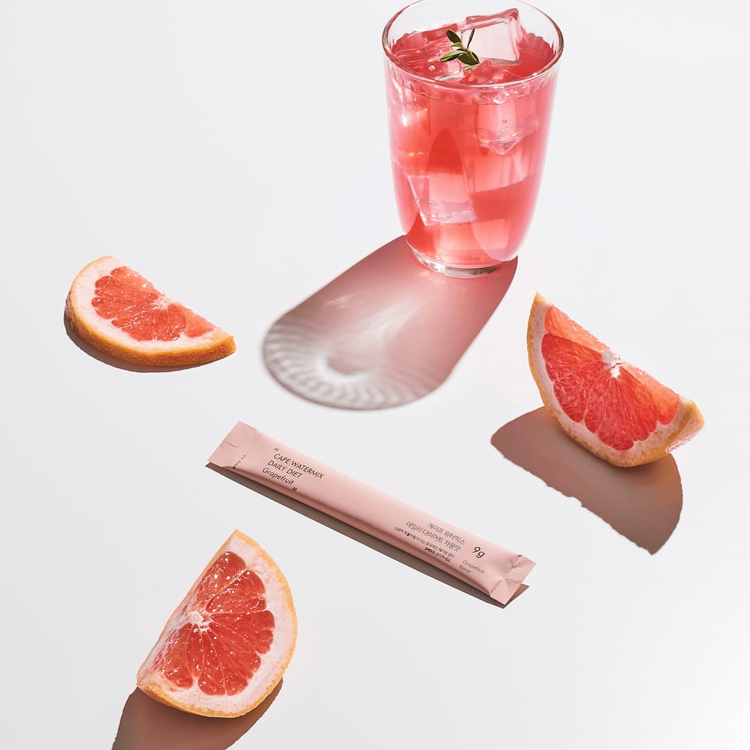 Ssunsu's CAPE Watermix Daily Diet Drink in its sachet, laid out next to a glass of it, and sliced grapefuits