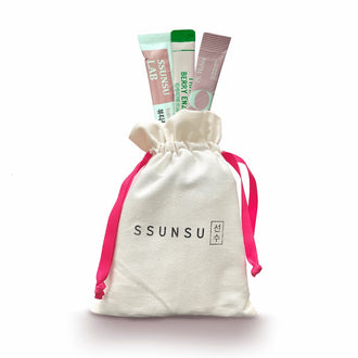 Ssunsu's Stay Healthy and Glowy Travel Kit with one sachet each of its three components sticking out of the white drawstring bag