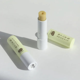 Two sticks of Whamisa Organic Fruits Multi-Balm on a white table, one opened and one closed