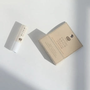A stick of Whamisa Organic Seeds Lip Balm on a white table, and its pink packaging box