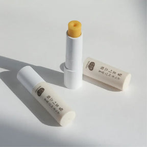 Two sticks of Whamisa Organic Seeds Lip Balm on a white table, one opened and one closed